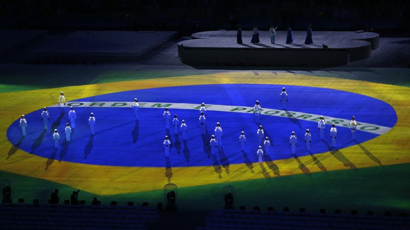 Um coro de crianças canta o hino do Brasil. Espalhadas pela bandeira brasileira, as crianças representam as estrelas do símbolo do país. Foto: Michael Reynolds/EPA